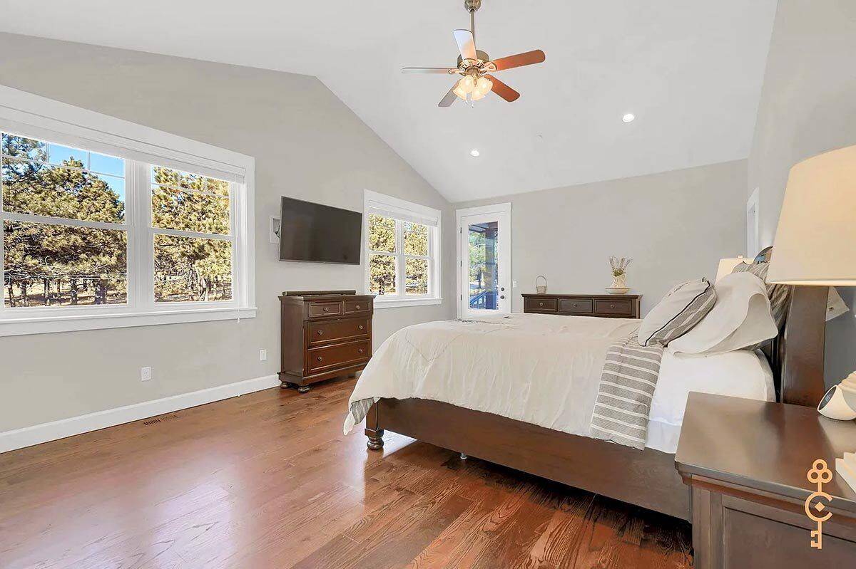 Primary bedroom with wooden furnishings, a wall-mounted TV, and a cathedral ceiling.