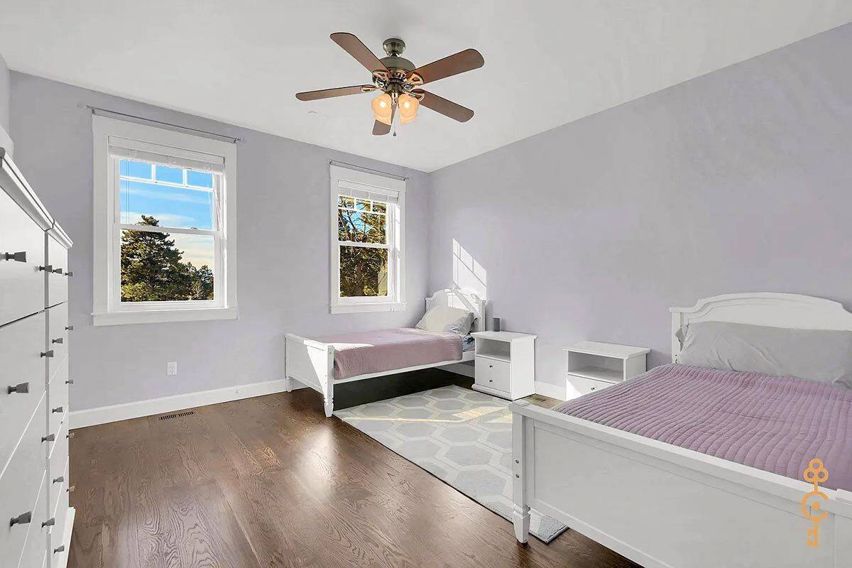 Secondary bedroom with two beds, white nightstands, and a patterned rug over the hardwood floor.