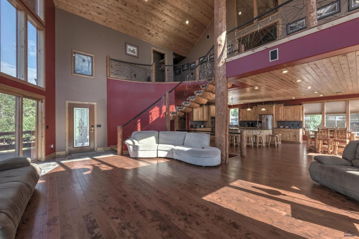 Living room with couches, staircase, glass walls and wood flooring.