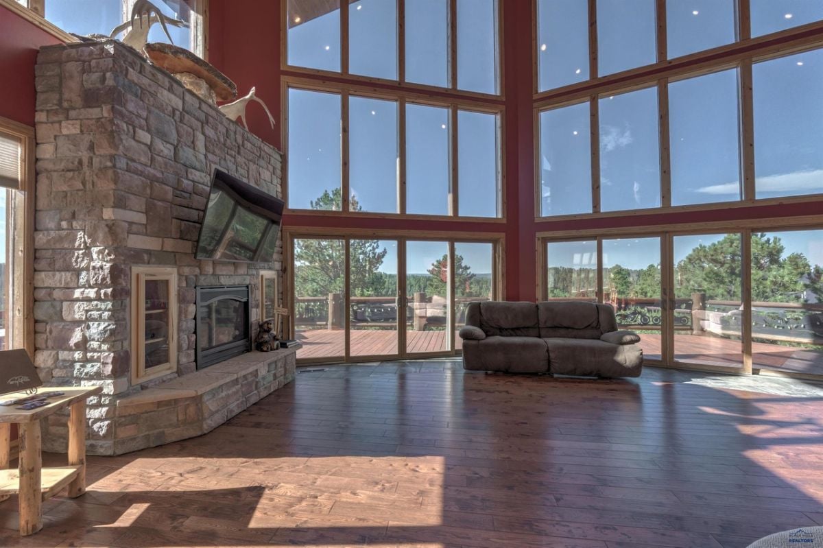 Living room with couches, TV, wooden floor, glass walls and a fireplace.