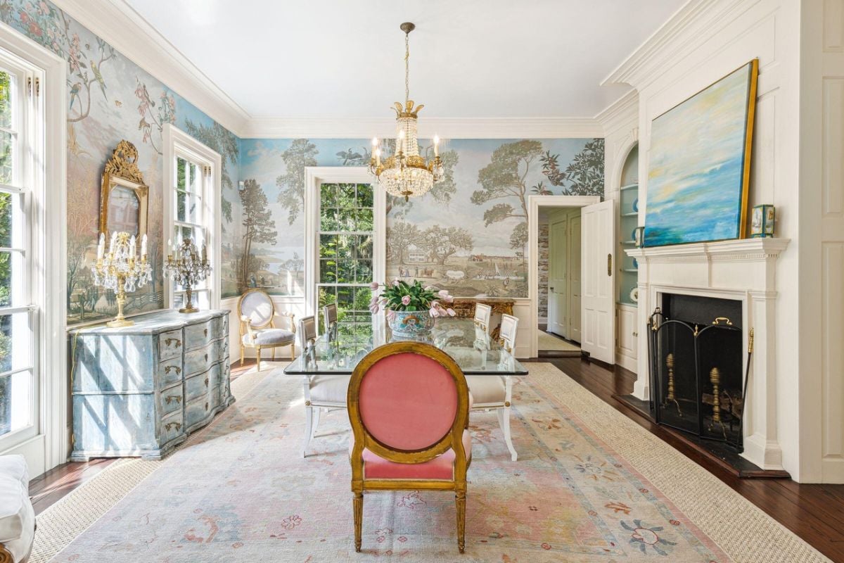 Dining room with a large glass table, chairs, chandelier and a fireplace.