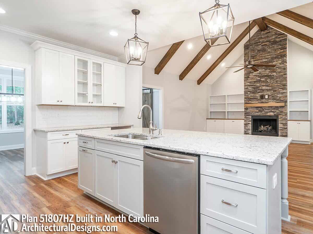 Kitchen island with a sink and dishwasher overlooking the great room.