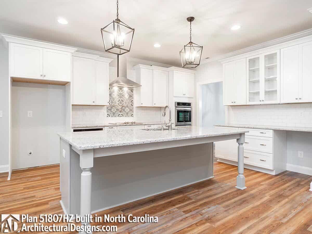 Kitchen with white cabinetry, granite countertops, and a center island topped with caged pendants.