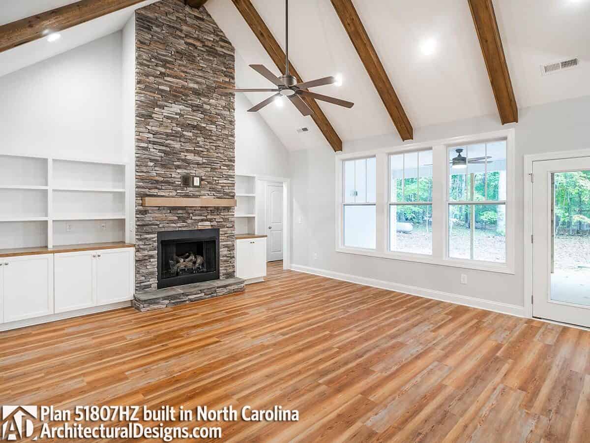 Great room with a stone fireplace, white built-ins, and a cathedral ceiling highlighted by exposed beams.