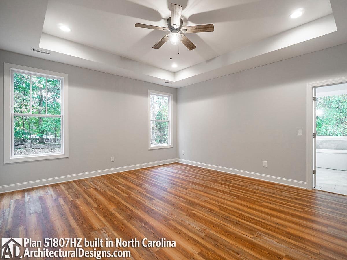 Primary bedroom with hardwood flooring, a tray ceiling, and outdoor access.