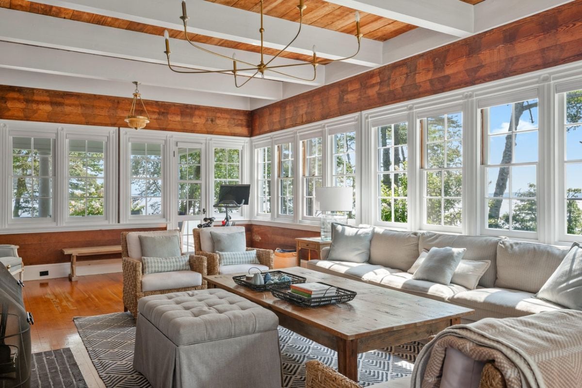 Living room with couches, rug, chandelier, wood flooring and glass windows.