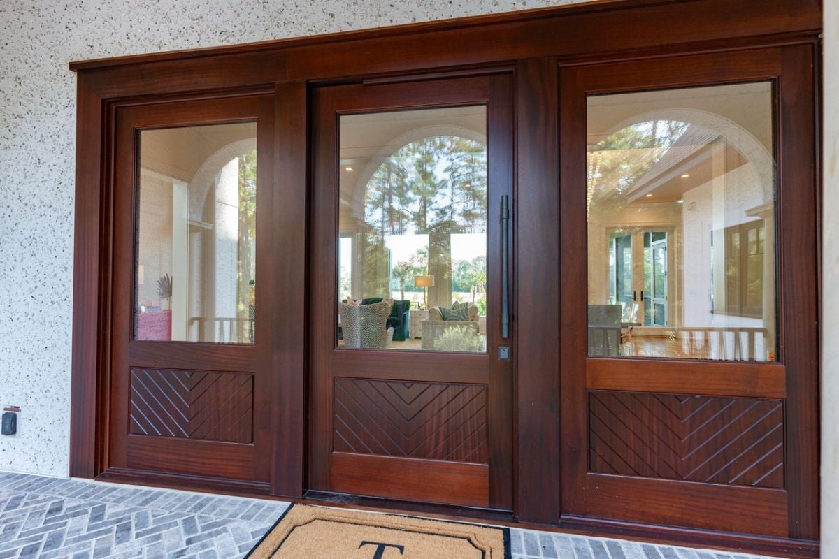 Front entry with a wooden door and a doormat.