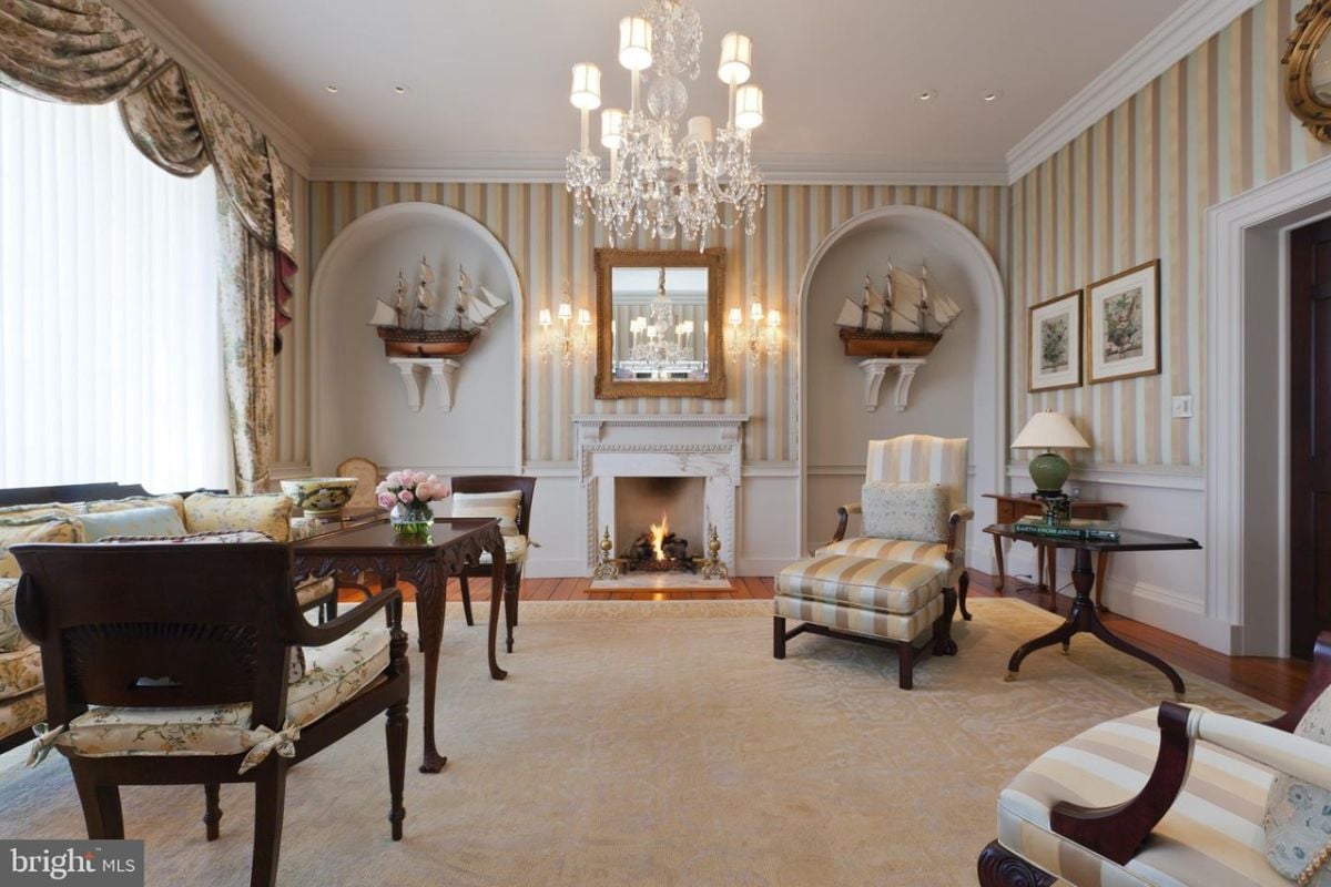 Living room with wooden floors, couches, chandelier. large rug and a fireplace.
