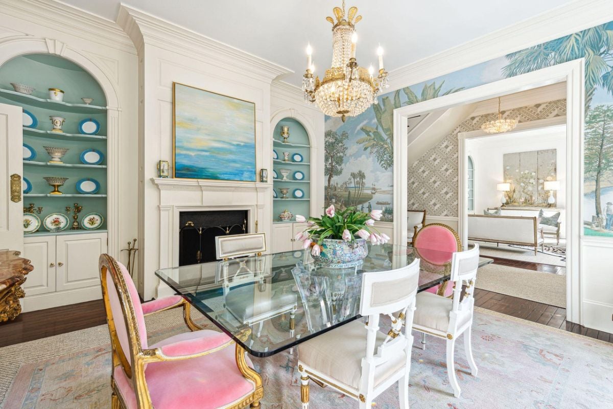 Dining room with a large glass table, chairs, chandelier and a fireplace.