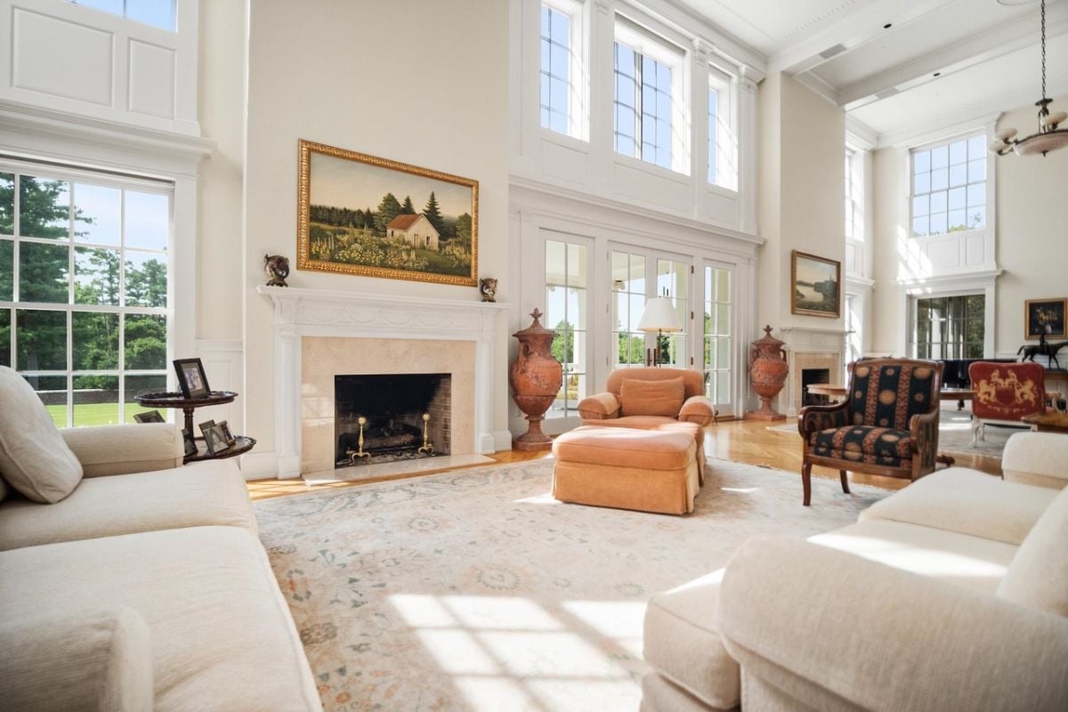Living room with couches, high ceilings, glass windows and a fireplace.