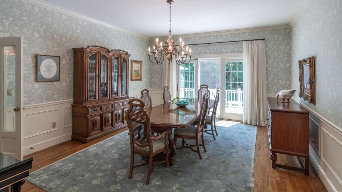 Dining room with a large table, chairs, chandelier, large rug and wood flooring.