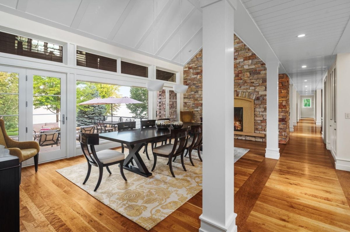 Dining room with a fireplace, glass doors, glass windows, a large wooden table and chairs.