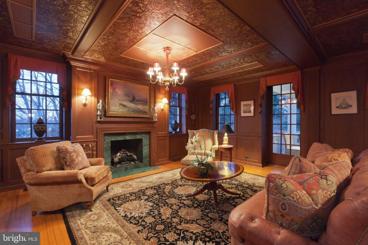 Living room with wooden floors, couches, chandelier, large glass windows and a fireplace.