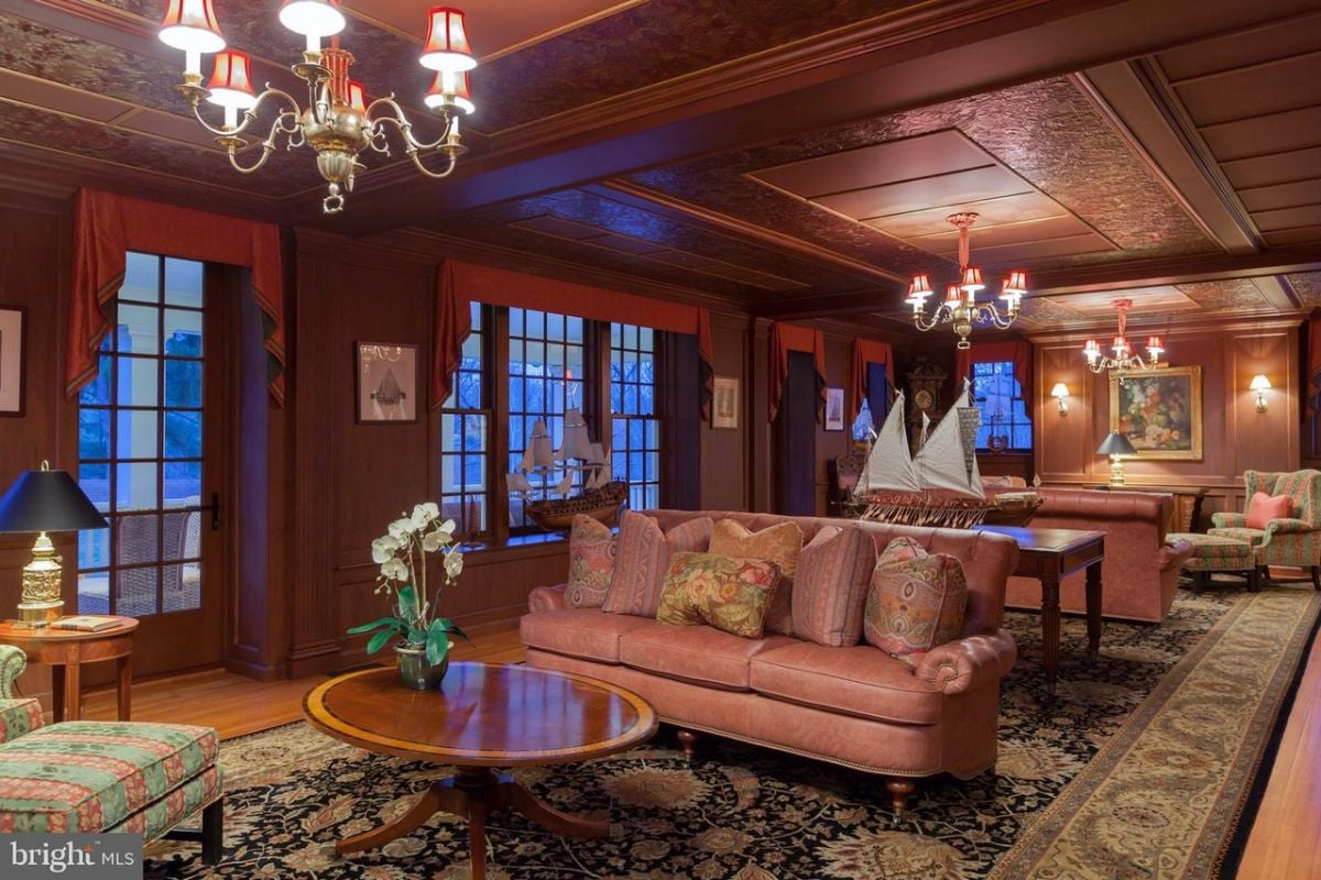 Living room with wooden floors, couches, chandeliers, a large rug, large glass windows and tables.