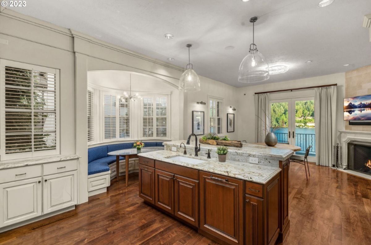 Kitchen with a large island, chandelier, wood flooring, custom lights, custom cabinets and a TV.