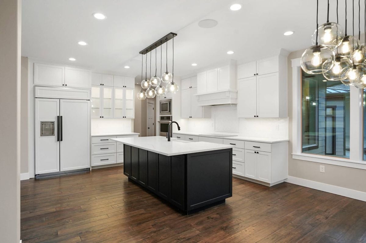 Kitchen with a large island, white cabinets, custom lights and wood floors.