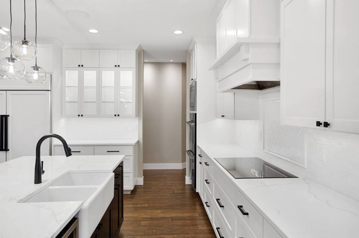 Kitchen with a sink, white cabinets, custom lights and wood floors.