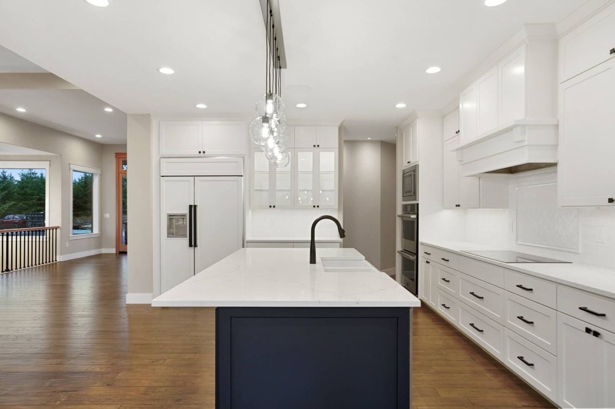 Kitchen with a large island, white cabinets, custom lights and wood floors.