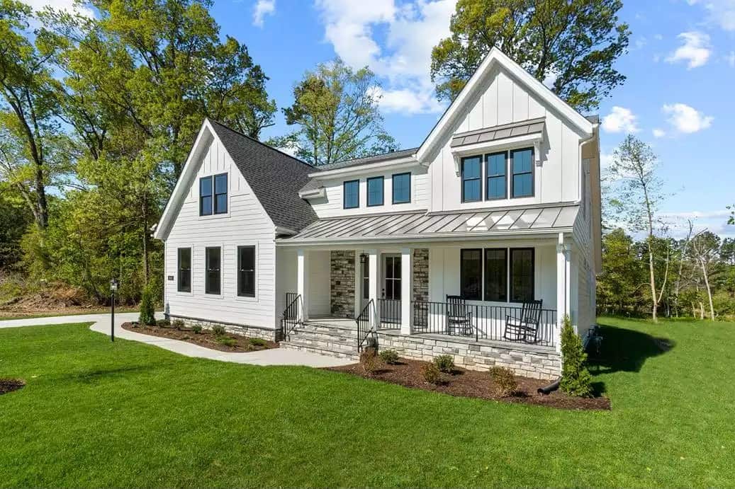 Front-right view with gable rooflines, a stone base, and a covered porch with a couple of rocking chairs.