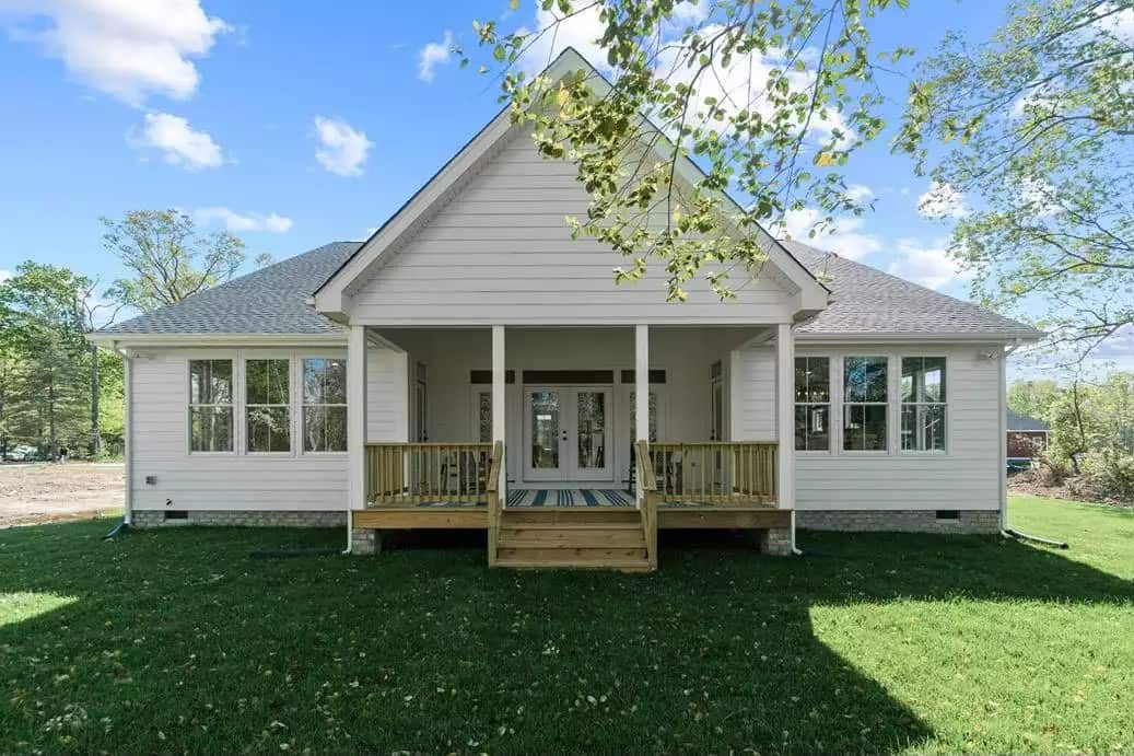 Rear view with a covered porch bordered with white columns and wooden railings.