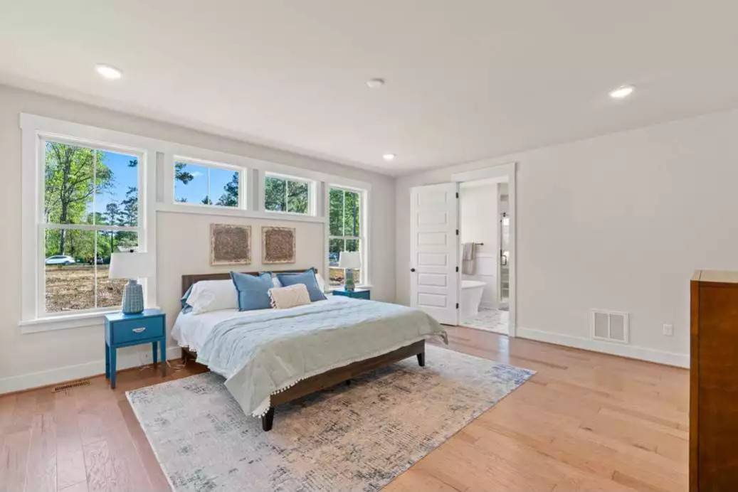 Primary bedroom with an ensuite bath, blue nightstands, and a wooden bed over the distressed area rug.