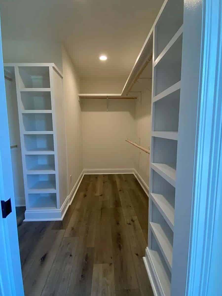 Primary walk-in closet with white built-ins and a hardwood floor.