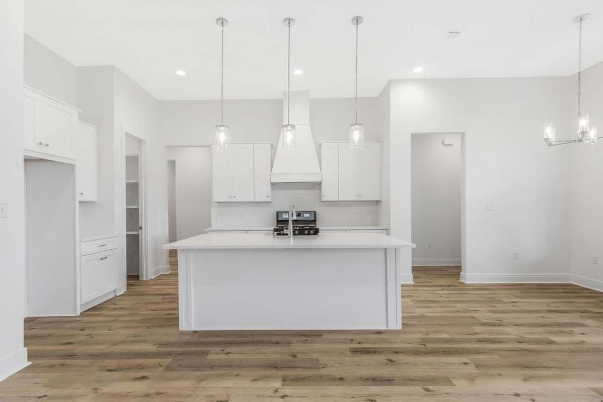 Kitchen with white cabinets and a matching island illuminated by glass pendants.