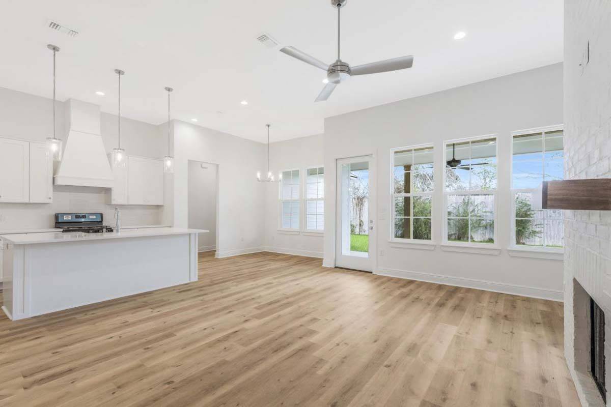 An open layout view of the great room, kitchen, and dining area brightened by rear windows.