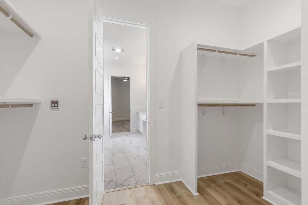Primary walk-in closet with ample storage and a hardwood floor.