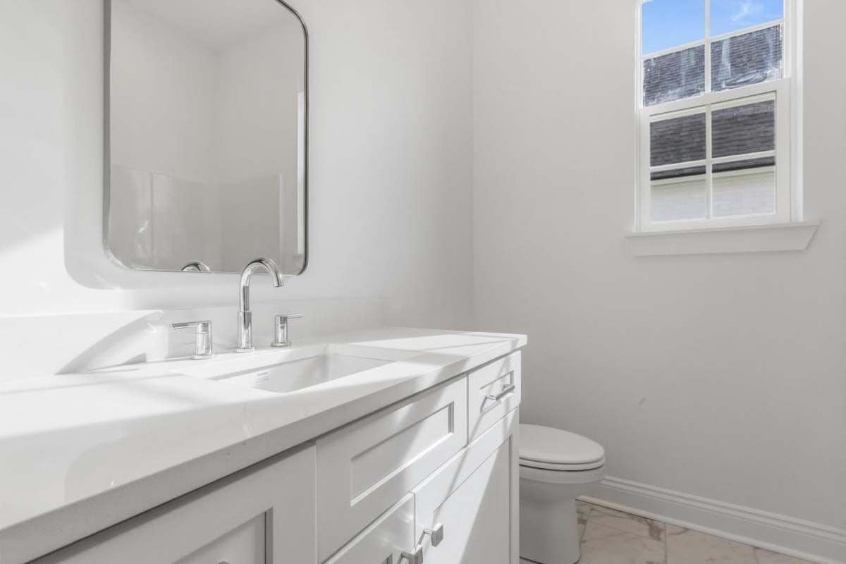 Bathroom with a toilet and a white vanity paired with a chrome-framed mirror.