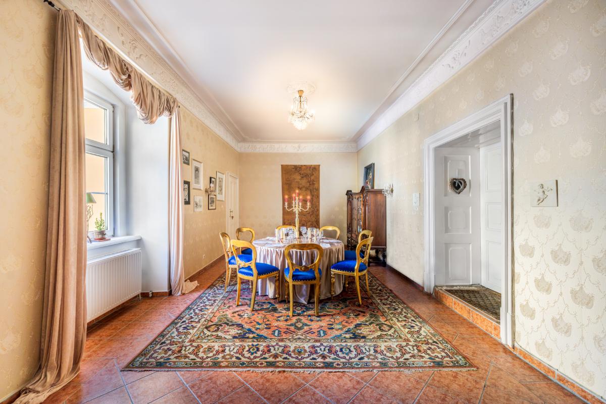 Dining room with a table, chairs, chandelier, large rug and glass windows.