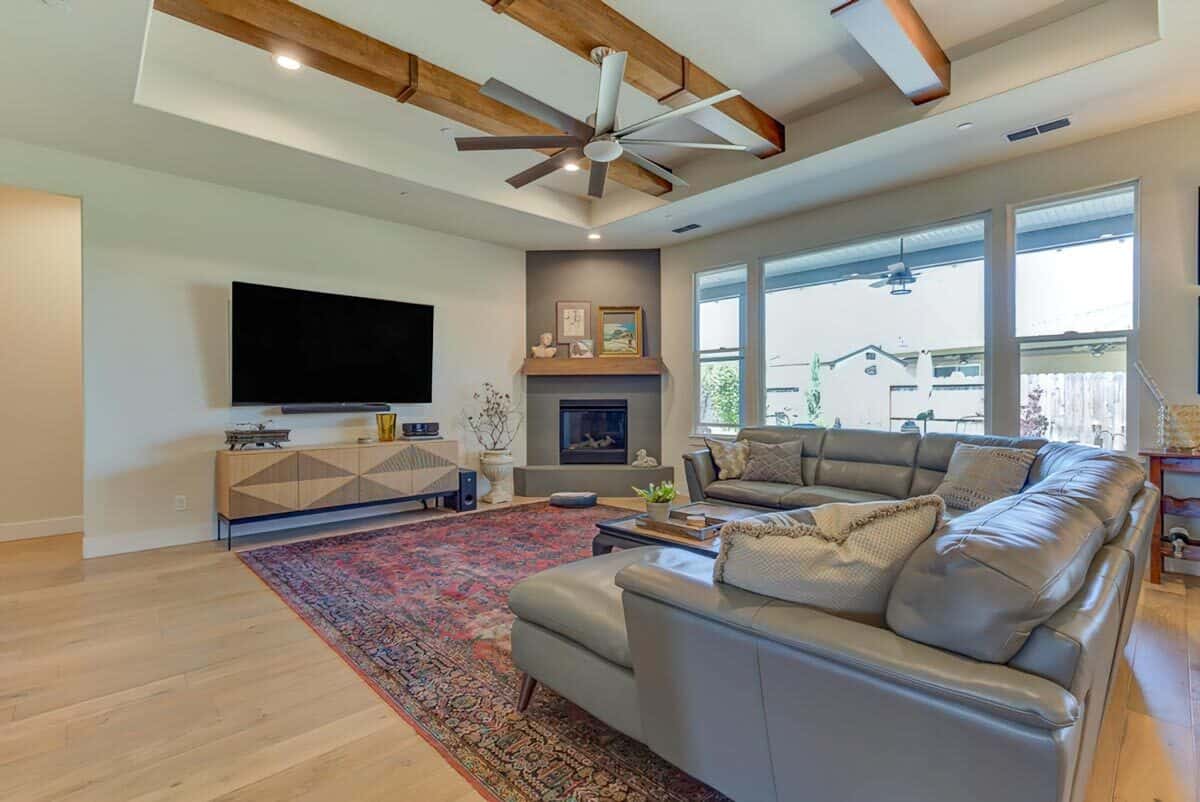 Great room with a sectional sofa, a corner fireplace, a wall-mounted TV, and a tray ceiling accentuated with exposed beams.