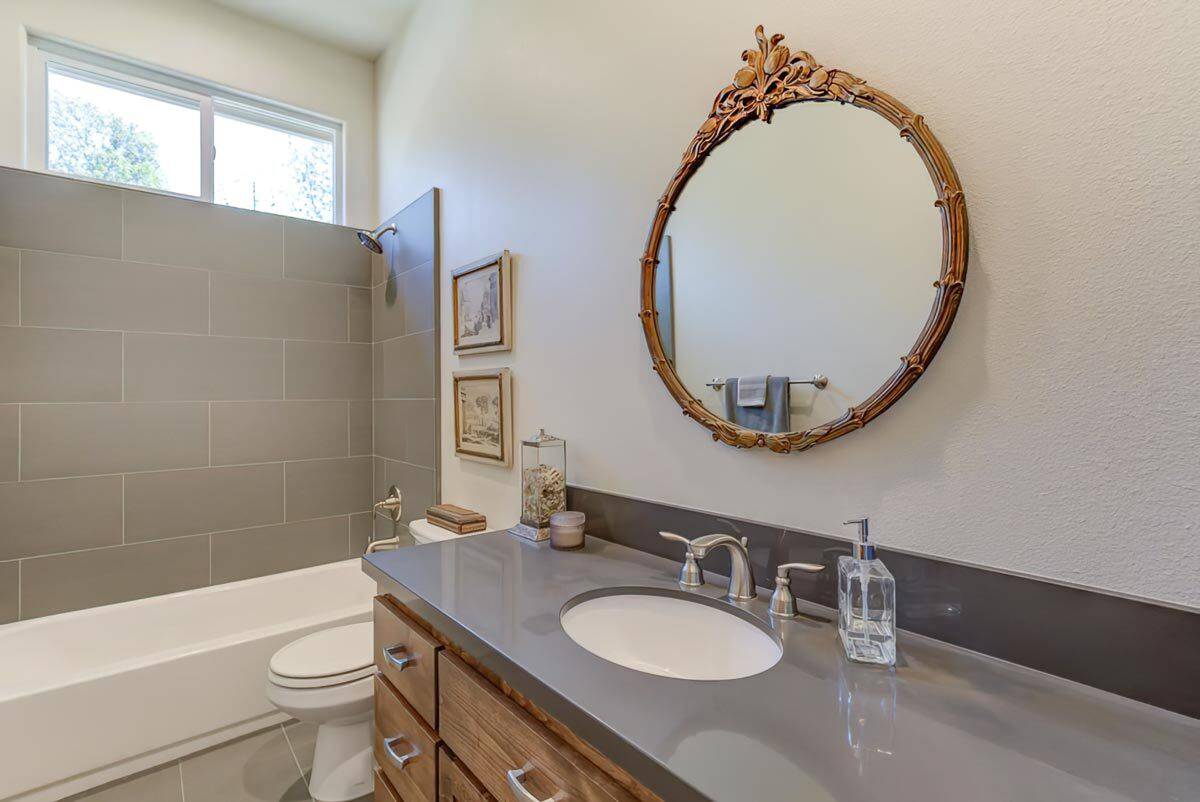 Bathroom with a tub and shower combo, a toilet, and a sink vanity adorned with a decorative mirror.