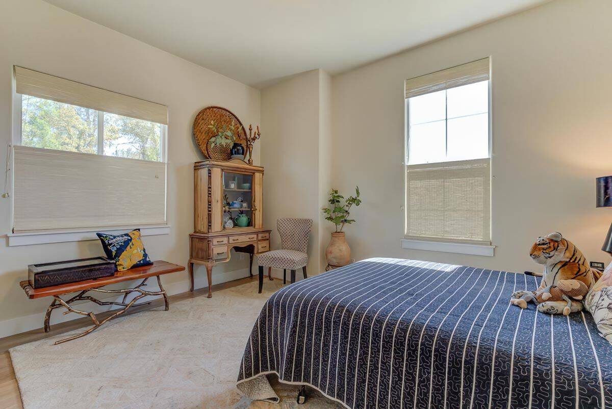 Bedroom with a platform bed, a wingback chair, and a wooden bench under the white-framed windows.