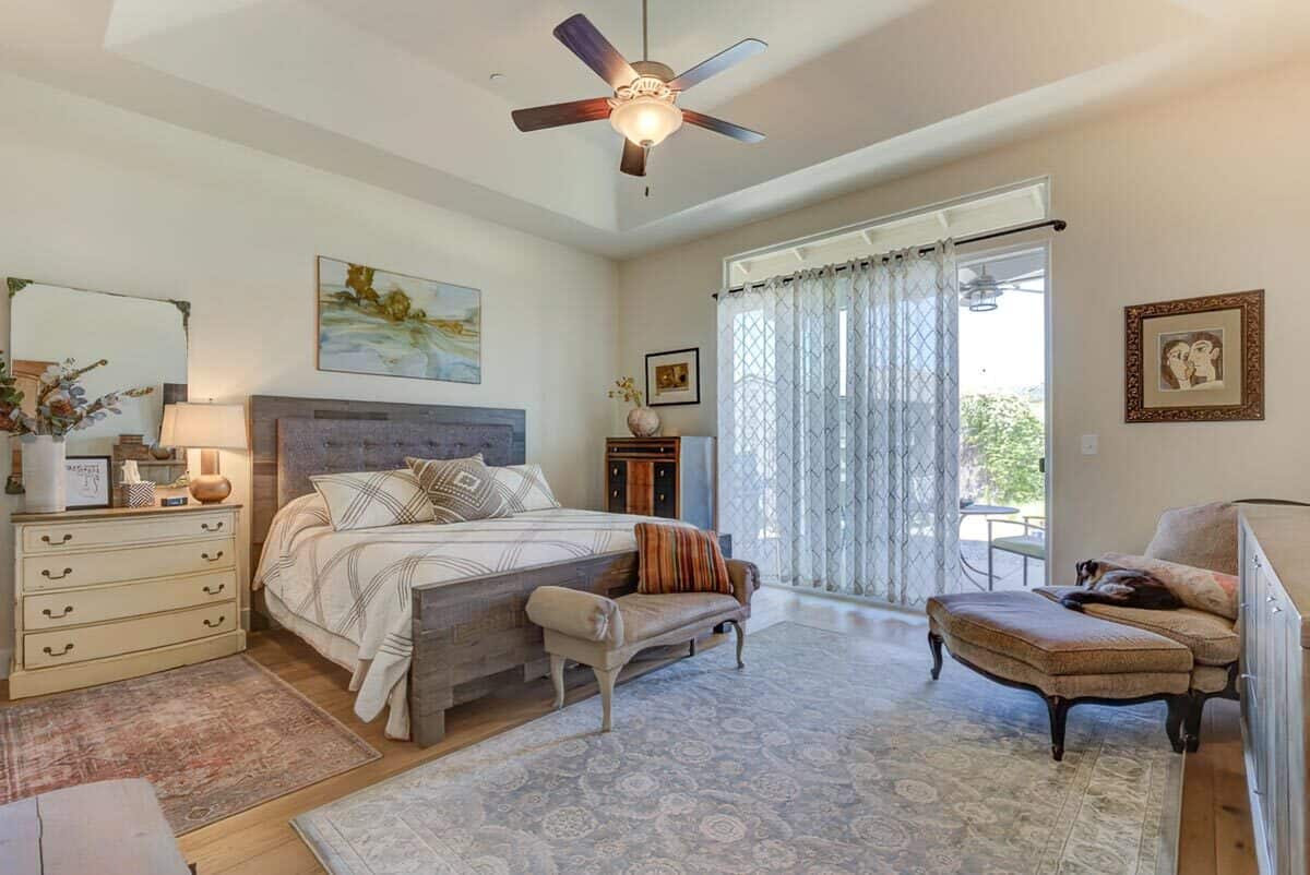 Primary bedroom with a tray ceiling, a traditional lounge chair, and a tufted bed complemented with a chaise lounge on its end.