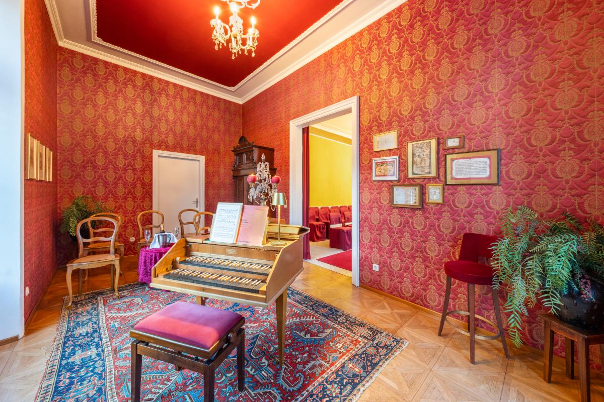 Music room with a piano, chairs, chandelier and a large rug.