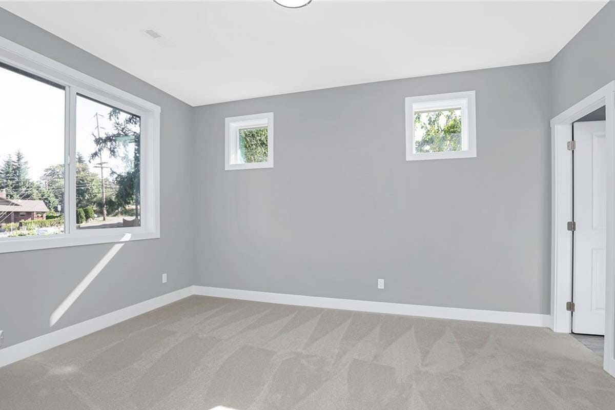Bedroom with a carpeted floor, gray walls, and white-framed windows.