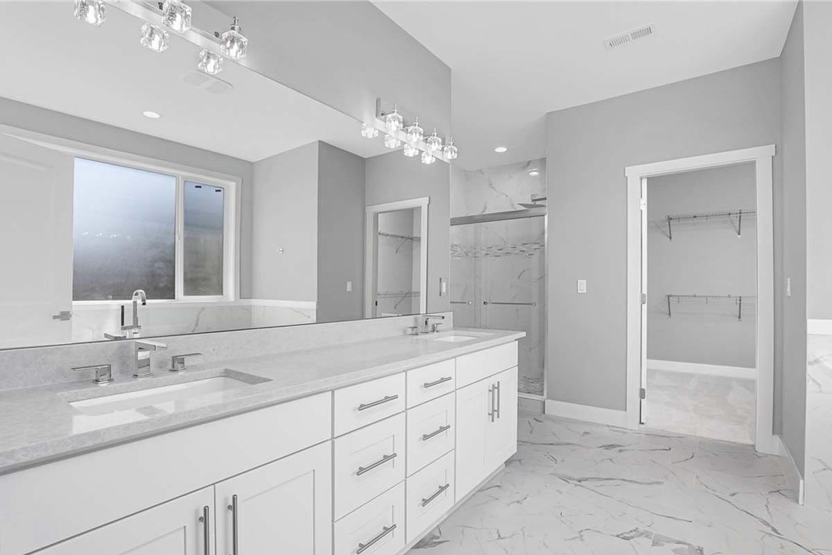 Primary bathroom with a dual sink vanity, a tiled shower, and a walk-in closet.