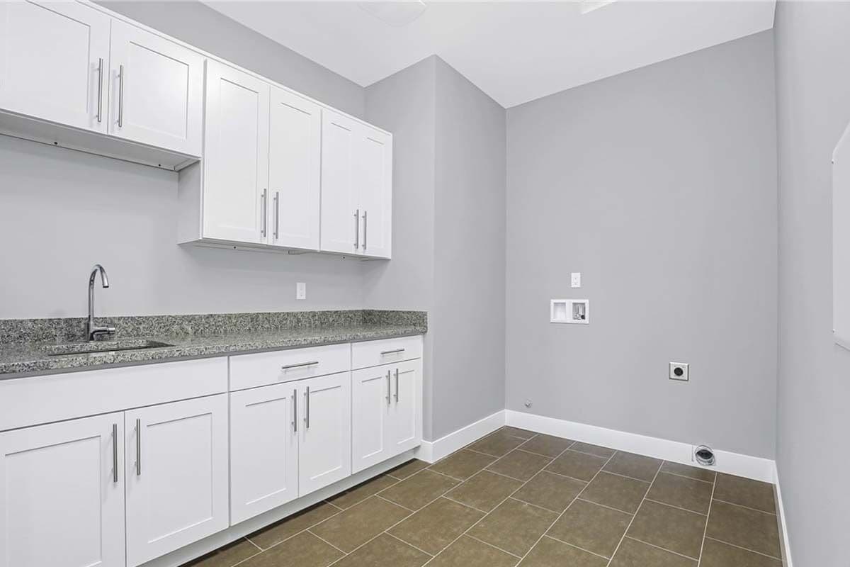 Laundry room with white cabinets and a granite counter fitted with a sink.
