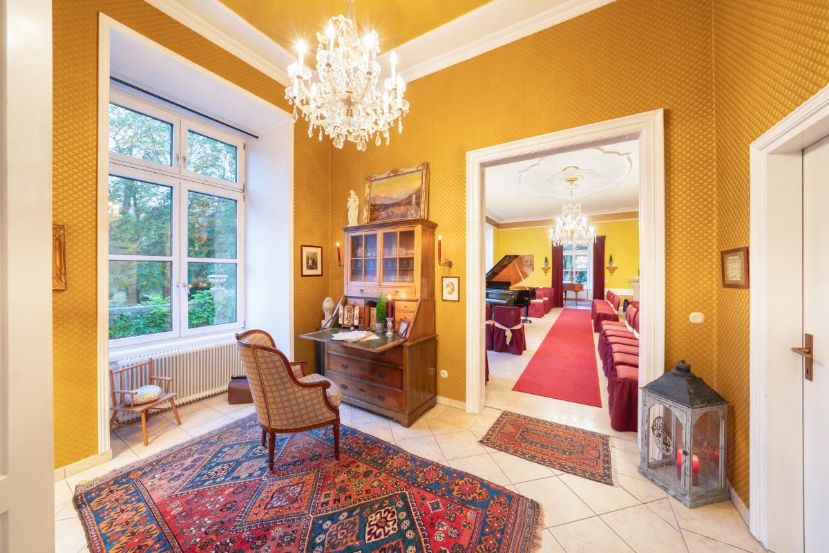 Sitting area with a chair, chandelier, glass windows and a large rug.