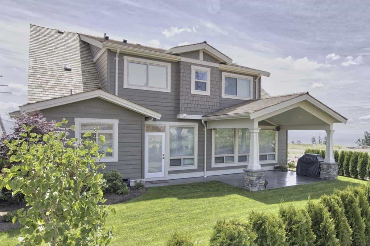 Rear view of the house with mixed sidings, gable rooflines, and a covered patio supported by stone base columns.