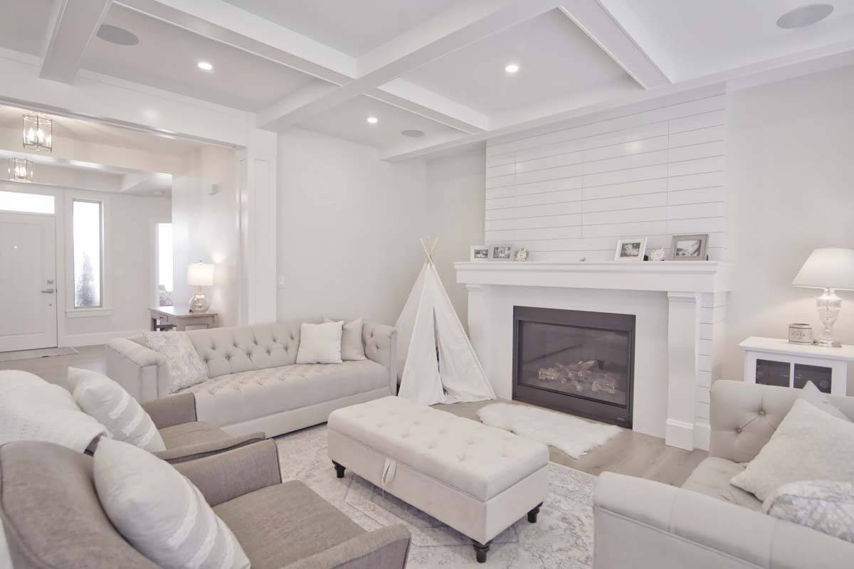 Great room with tufted sofas, a matching ottoman, and a fireplace under a coffered ceiling.