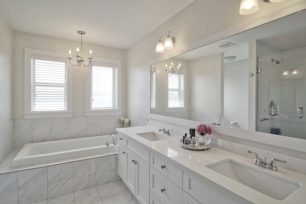 Primary bathroom with a dual sink vanity and a drop-in bathtub under white-framed windows.
