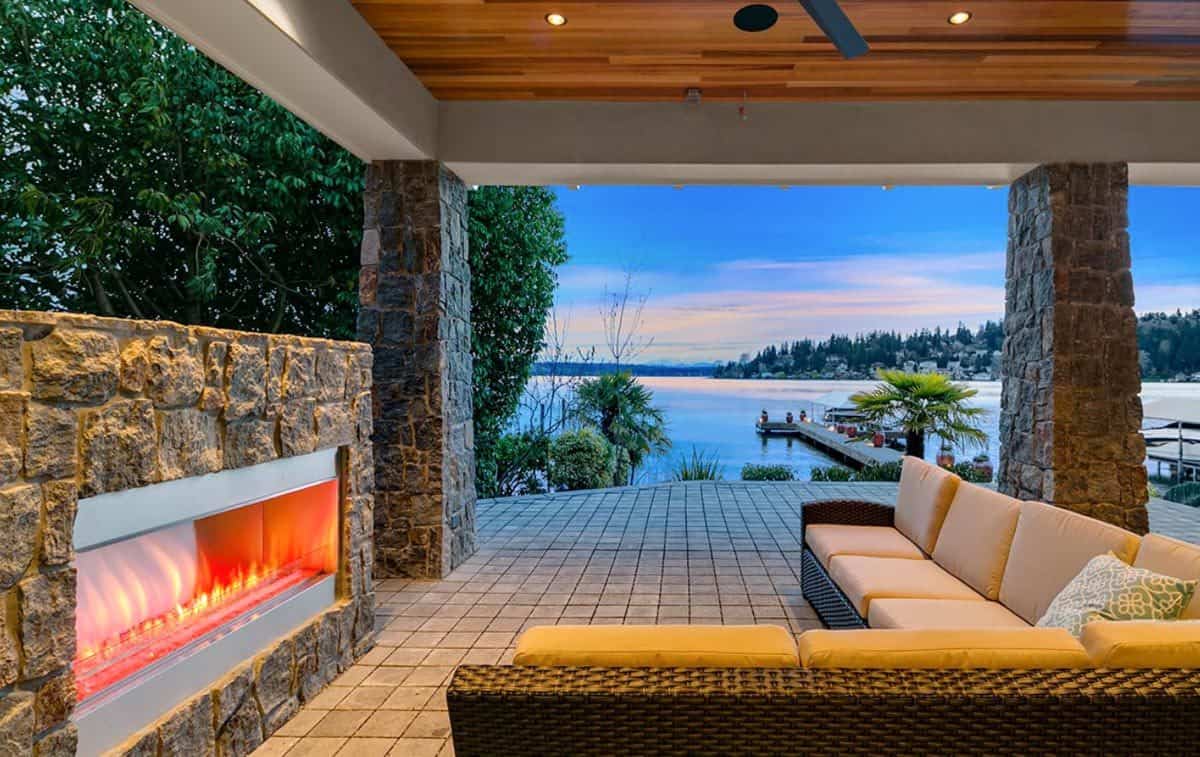 The covered patio includes a wicker sectional sofa and a large stone fireplace.