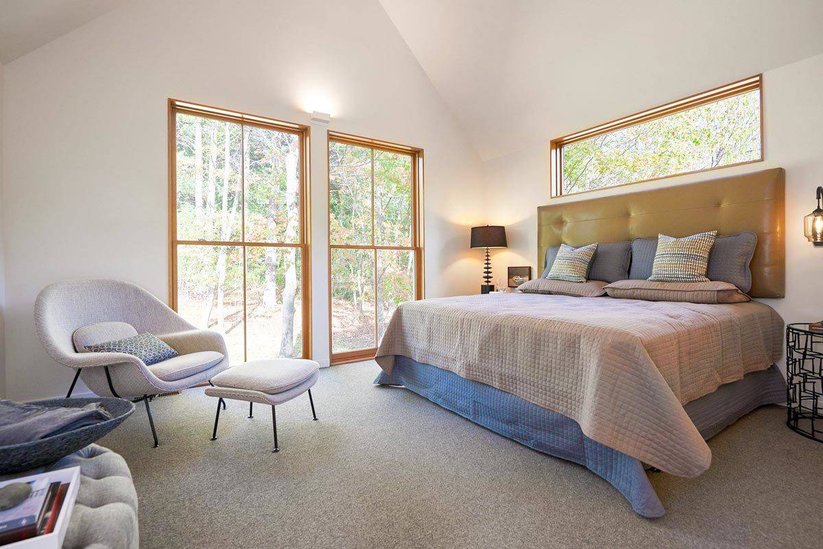 Primary bedroom with a cathedral ceiling, a tufted bed, and tall windows overlooking the backyard.