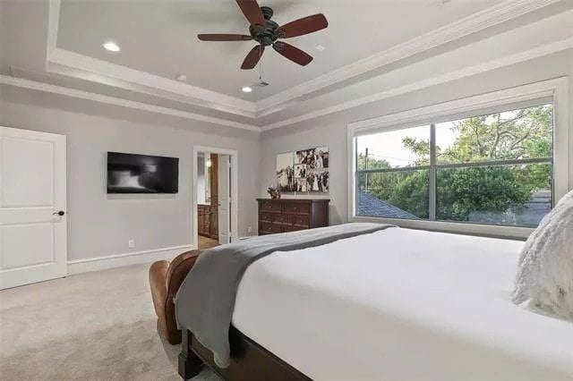 Primary bedroom with a wooden bed, a wall-mounted TV, and a traditional fan mounted on the tray ceiling.