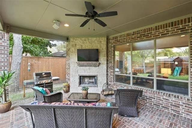Outdoor living with wicker seats, a BBQ grill,. and a corner fireplace with a TV on top.
