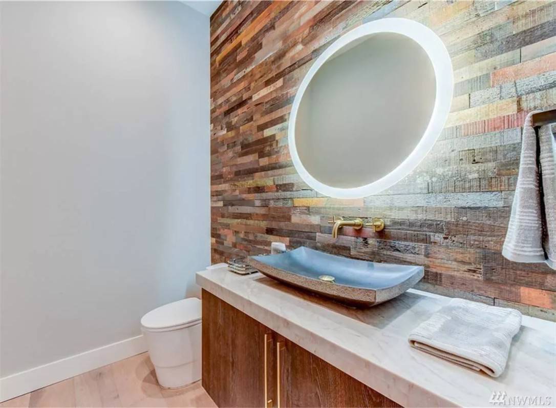 Powder room with a vessel sink and a brick accent wall adorned with an illuminating mirror.