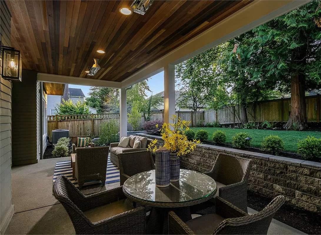 Covered deck with wicker cushioned chairs and a matching dining set under a wood-paneled ceiling.