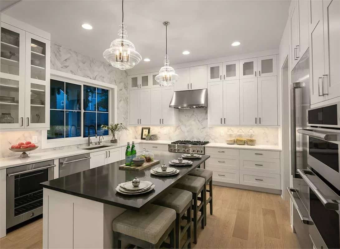 Kitchen with white cabinetry, modern appliances, and a center island topped with glass pendants.